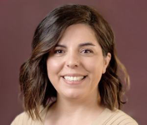 Professional headshot of Darya Anoshei, International Scholar Operations Specialist. She is shown with shoulder-length wavy dark hair, facing the camera against a softly blurred burgundy background. The person is wearing a light-colored top and is centered in the frame, with the image cropped from the shoulders up and evenly lit.